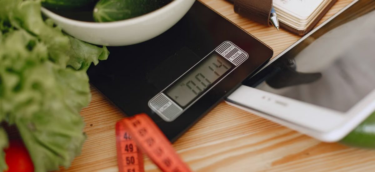 A bowl of fresh vegetables on a kitchen scale with measurement tools, depicting a healthy lifestyle.