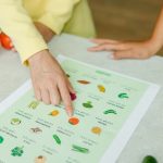 Close-up of hands pointing to a vegetable nutrition chart with fresh tomatoes on the table.